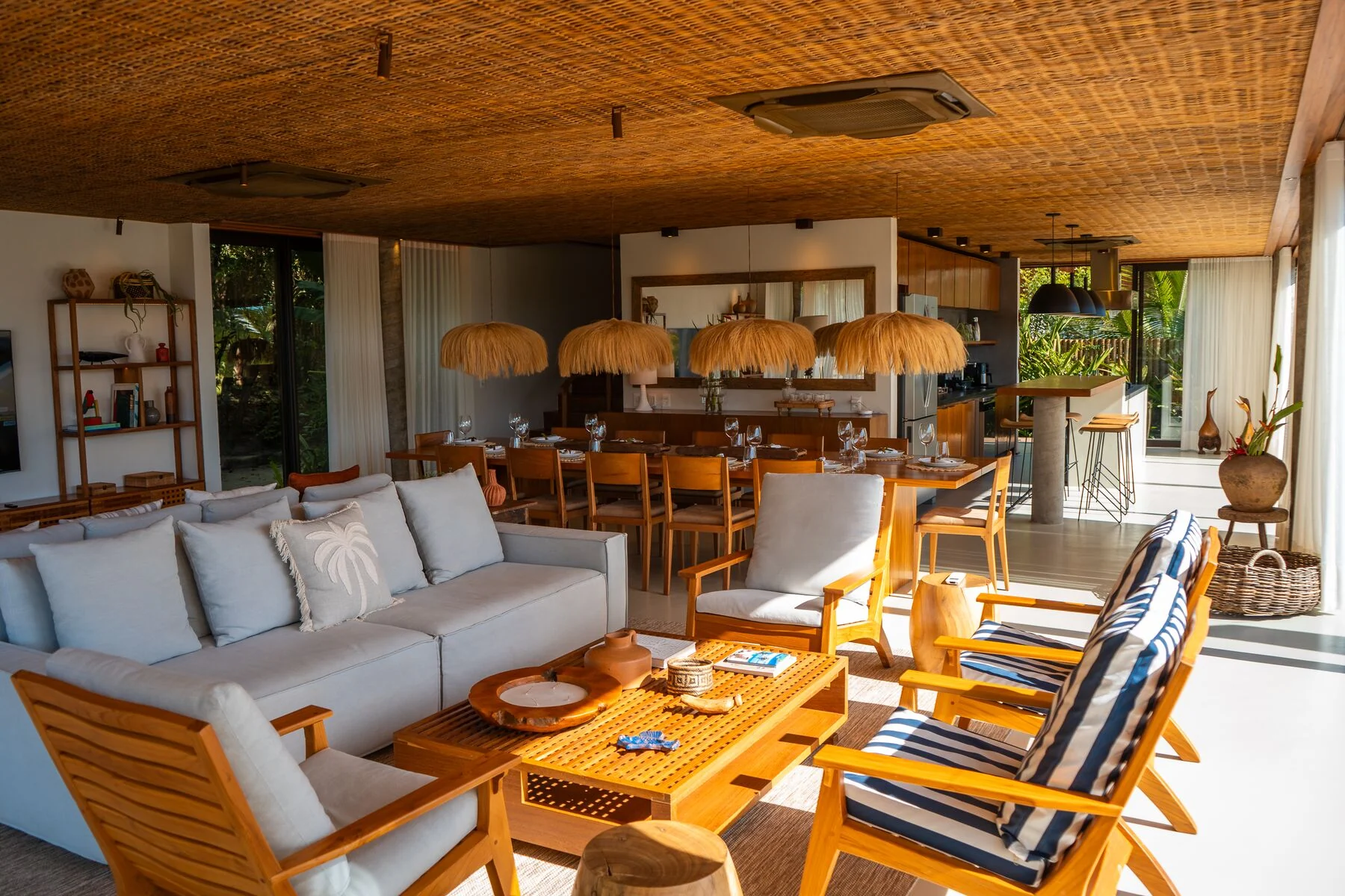 Sala e jantar abertos da Casa 101 sob teto de palha trançada